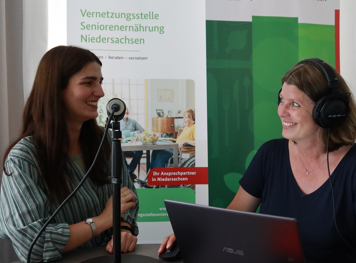 2 Frauen mit Kopfhörer und Mikrofon lächeln sich an